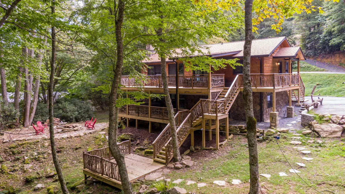 A spacious wooden deck surrounded by trees and natural rock formations, featuring vibrant red chairs arranged for outdoor relaxation and gatherings. The deck offers ample room for group seating, perfect for socializing against a backdrop of lush greenery.