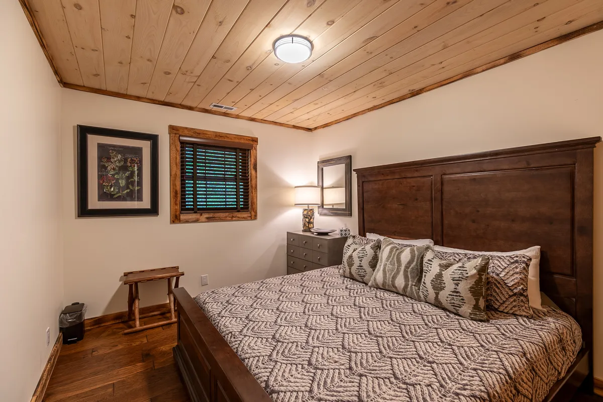 A serene guest bedroom featuring a bed with patterned bedding, a nightstand with a stylish lamp, and framed artwork on the wall. Morning sunlight gently fills the space, creating an inviting and restful environment.