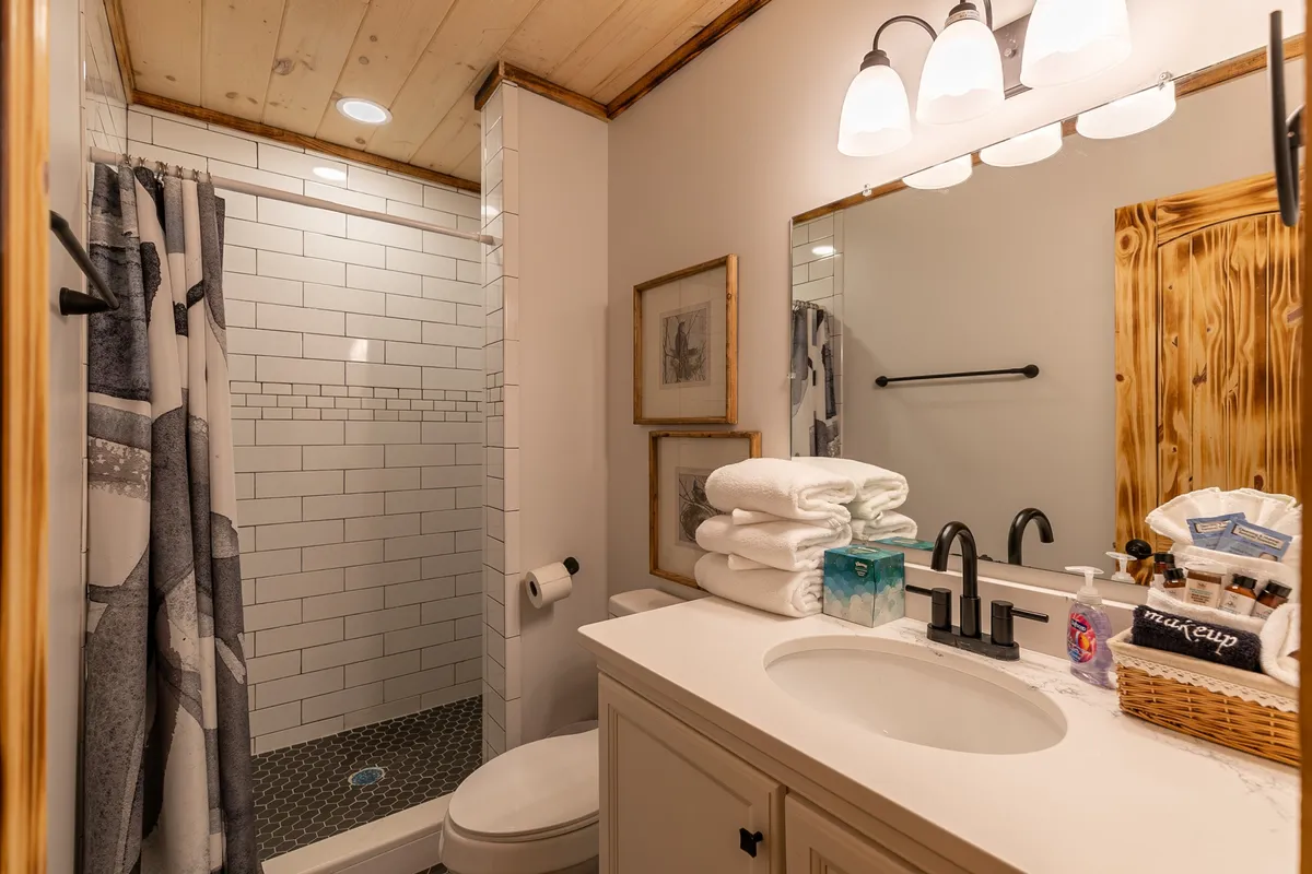 A luxurious bathroom with a spacious shower area, vanity with a large mirror, stacked fluffy towels, and framed artwork. The clean design and serene mood evoke a spa-like experience.
