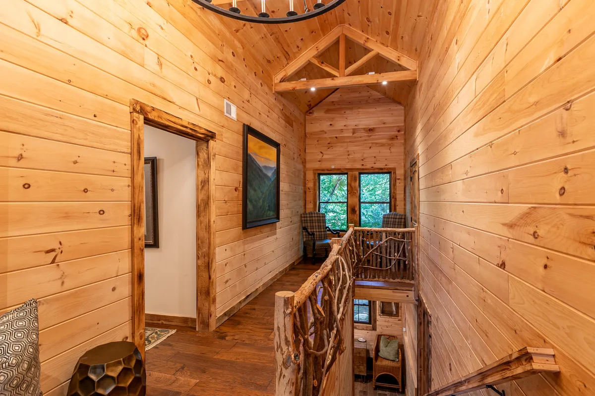 A cozy seating area with a wooden railing and large windows, artwork on the wall, and comfortable chairs. The expansive windows suggest scenic mountain vistas, evoking a sense of peaceful escape and connection with nature.