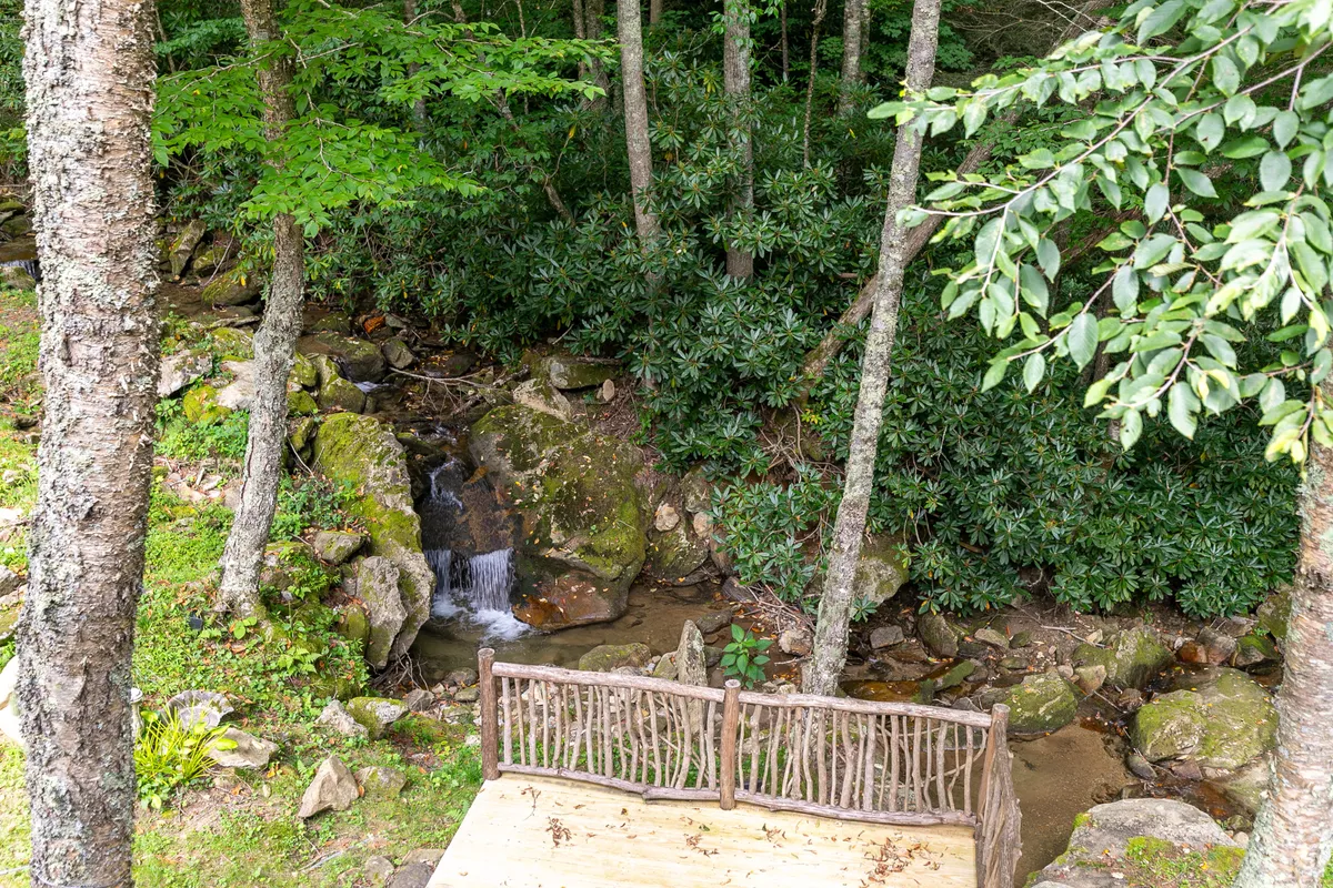 A beautiful natural waterfall beside a wooden bench, surrounded by lush greenery. The bench invites visitors to sit, relax, have a picnic, or simply enjoy the sights and sounds of nature. The setting is serene and ideal for family exploration.