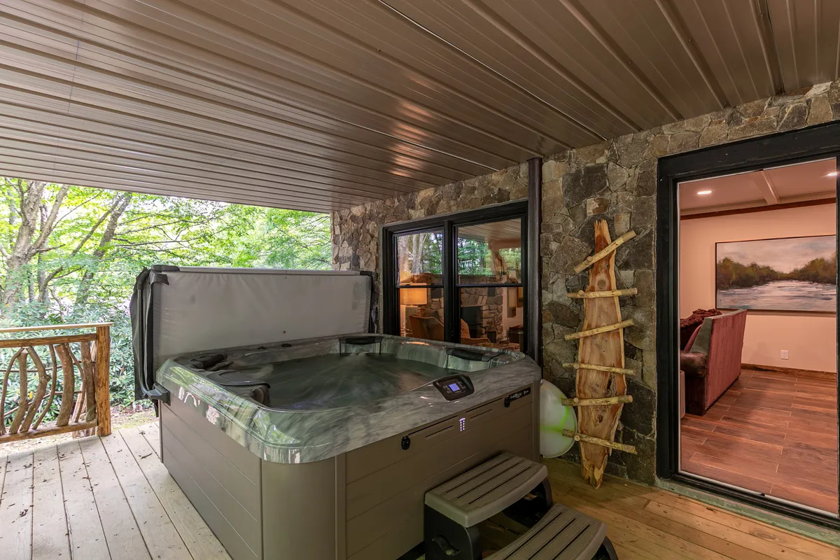 An inviting hot tub set against a rustic stone wall and wooden railing, with a glimpse of the outdoors through a window. The tranquil vibe suggests luxurious relaxation, perfectly in tune with the natural surroundings.