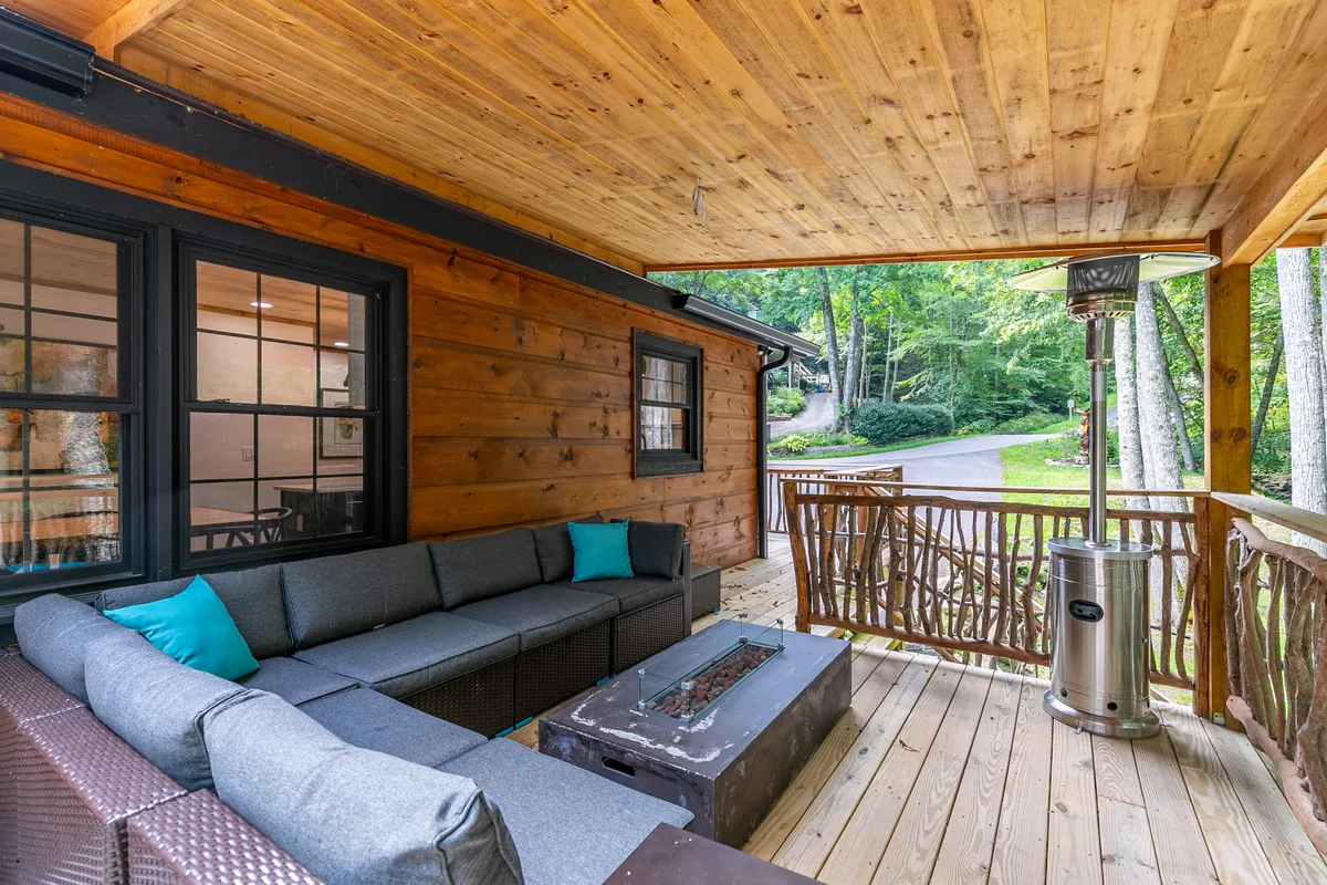 A welcoming outdoor seating area is arranged around a fire pit, complete with a comfy sofa, outdoor heater, and wooden railing. The setting is surrounded by trees, creating a private oasis for groups to gather and enjoy the mountain air.