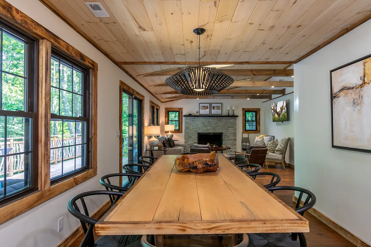 A rustic yet elegant dining area centers around a large wooden table, with a glowing fireplace set into the wall. A unique light fixture adds visual interest, and the setting is ideal for family gatherings, intimate dinners, or celebratory meals, seamlessly connecting the dining experience to the warmth of the main living area.