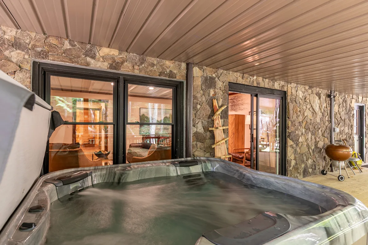 This image highlights a serene hot tub area with large windows, a stone wall, and comfortable seating. The windows connect the space to the outdoors, suggesting a tranquil and luxurious experience with views of nature.