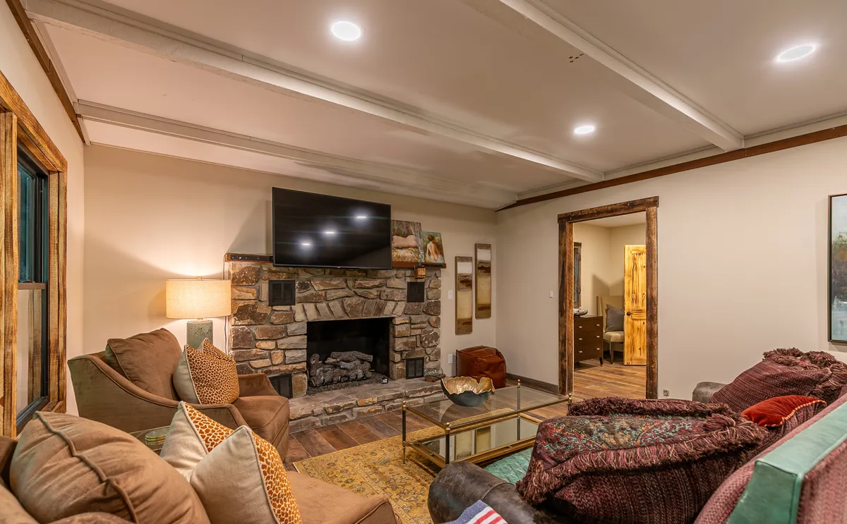 A cozy living area centered around a stone fireplace, with large TV, comfortable sofas, and wooden doors that may lead outside. The ambiance is warm and inviting, perfect for gathering after a day of seasonal adventures.